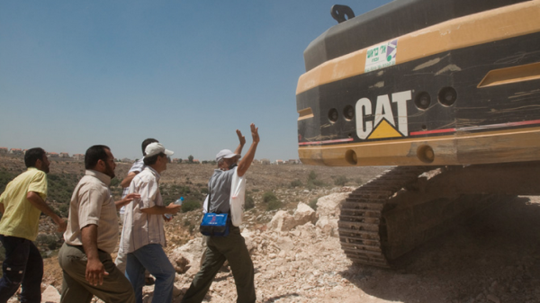 Activists in the West Bank village of Ni'lin block a Caterpillar excavator used in the construction of the apartheid wall