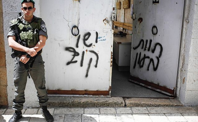 Border Police guard stands next to anti-Christian graffiti 